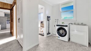 Een praktische wasruimte met een voorlader wasmachine en droger, een klein wastafeltje en een raam met uitzicht.