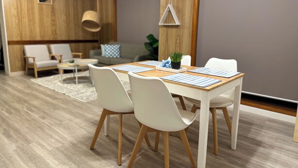 Een moderne eetruimte met een houten tafel, witte stoelen en een grijze bank op de achtergrond.