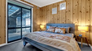 Een slaapkamer met een bed, twee bedlampen, een houten wand en een glazen schuifdeur die uitkomt op een buitengebied.