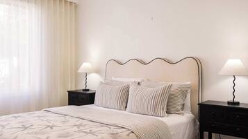 A hotel room with a bed, two bedside tables, a lamp on each table, and a window with curtains.