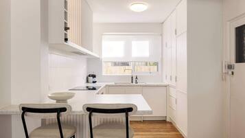 A modern kitchen with white cabinetry, a central island, two bar stools, and a window providing natural light.