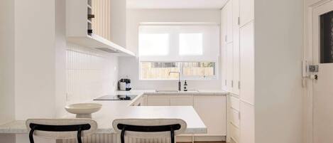 A modern kitchen with white cabinetry, a central island, two bar stools, and a window providing natural light.