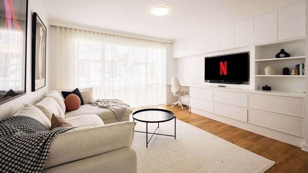 A modern living room with a sofa, a coffee table, a TV mounted on the wall, and a bookshelf.
