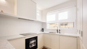 A modern kitchen with white cabinetry, a built-in oven, a dishwasher, and a window providing natural light.