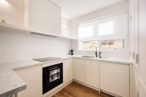 A modern kitchen with white cabinetry, a built-in oven, a dishwasher, and a window providing natural light.