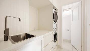 A laundry area with a washing machine and dryer, a stainless steel sink, and a white tiled wall.