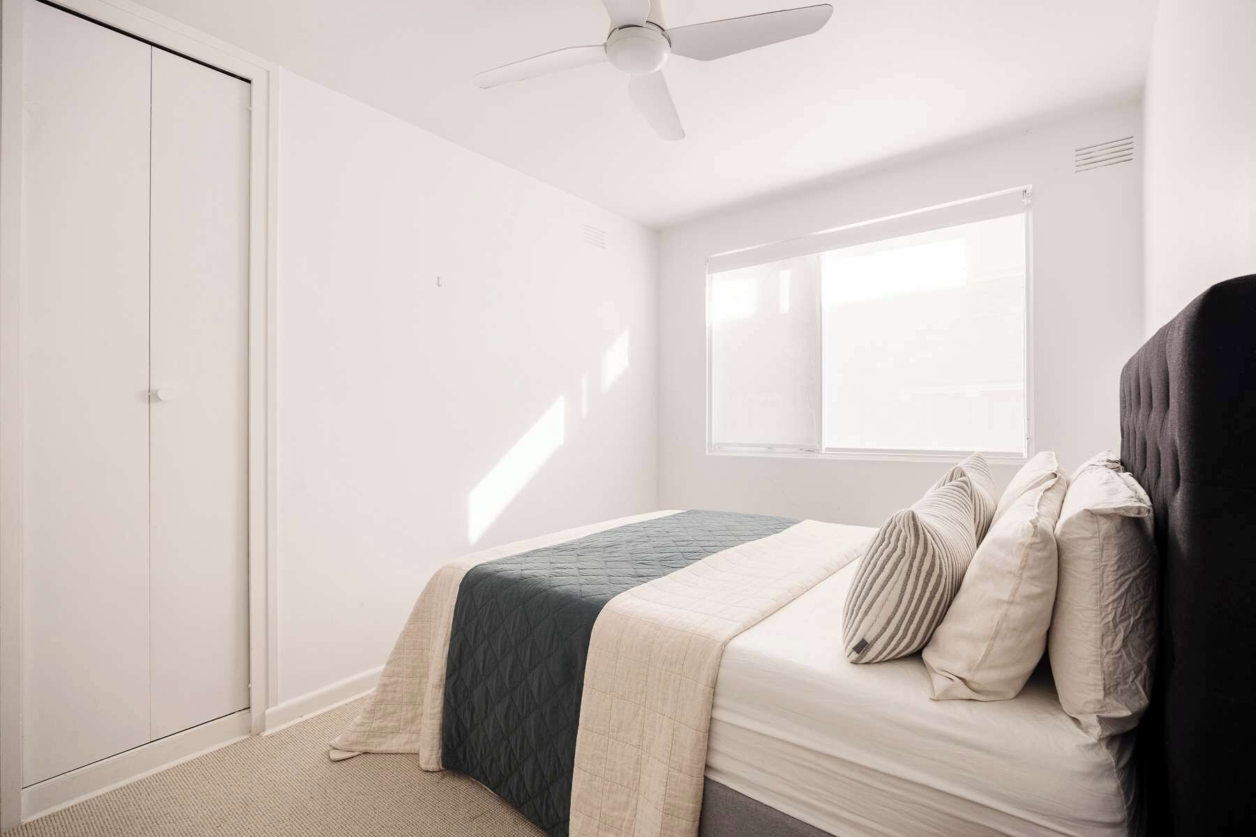 A bedroom with a bed, a window, a ceiling fan, and a wardrobe.