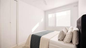 A bedroom with a bed, a window, a ceiling fan, and a wardrobe.