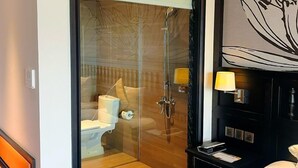 Una habitación de hotel moderna con ducha de vidrio, cama con cubrecama a rayas y una gran obra de arte colgada en la pared de una flor de loto.