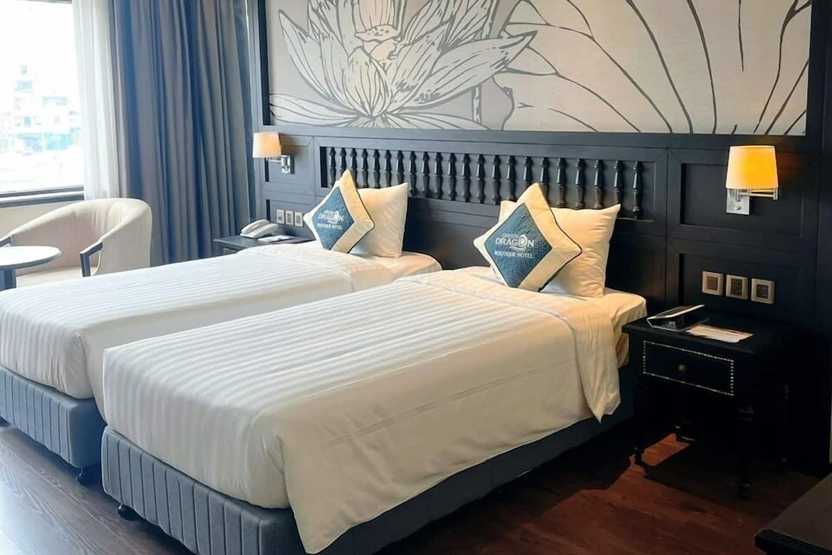 Habitación de hotel con dos camas, un escritorio, una silla y un mural grande en la pared.