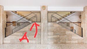 Een statige trap met een marmeren vloer en een centrale kolom, die leidt naar een hoger gelegen niveau.