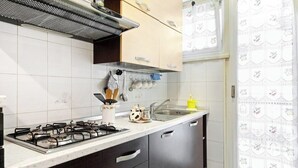 Een keuken met een gasfornuis, een roestvrijstalen spoelbak en houten keukenkastjes.