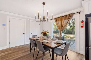 Ein Essbereich mit einer Chandelieber, einem für vier Personen gedeckten Tisch und Blick ins Freie.