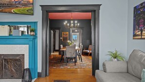 A modern living room with a fireplace, a dining area with a table and chairs, and a hallway leading to another room. - Walkable Historic District 1 Mi to Downtown Lou! (Jeffersonville)