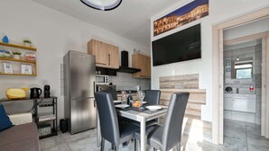 A modern kitchen with a dining area, featuring a stainless steel refrigerator, microwave, and oven, wooden cabinets, and a flat-screen TV mounted above the counter. - The Red House - Verona Holiday & Business (Verona)