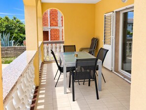 A balcony with a table and chairs, a view of a brick wall, and a sliding glass door.