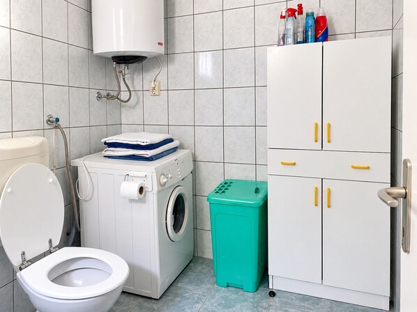 Une salle de bain équipée de toilettes, d’un lave-linge et d’un meuble avec des poignées jaunes.