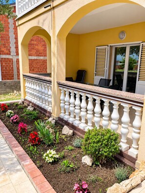 Un bâtiment jaune doté d’un balcon, d’un mur en briques et d’un jardin où poussent différentes espèces de plantes.