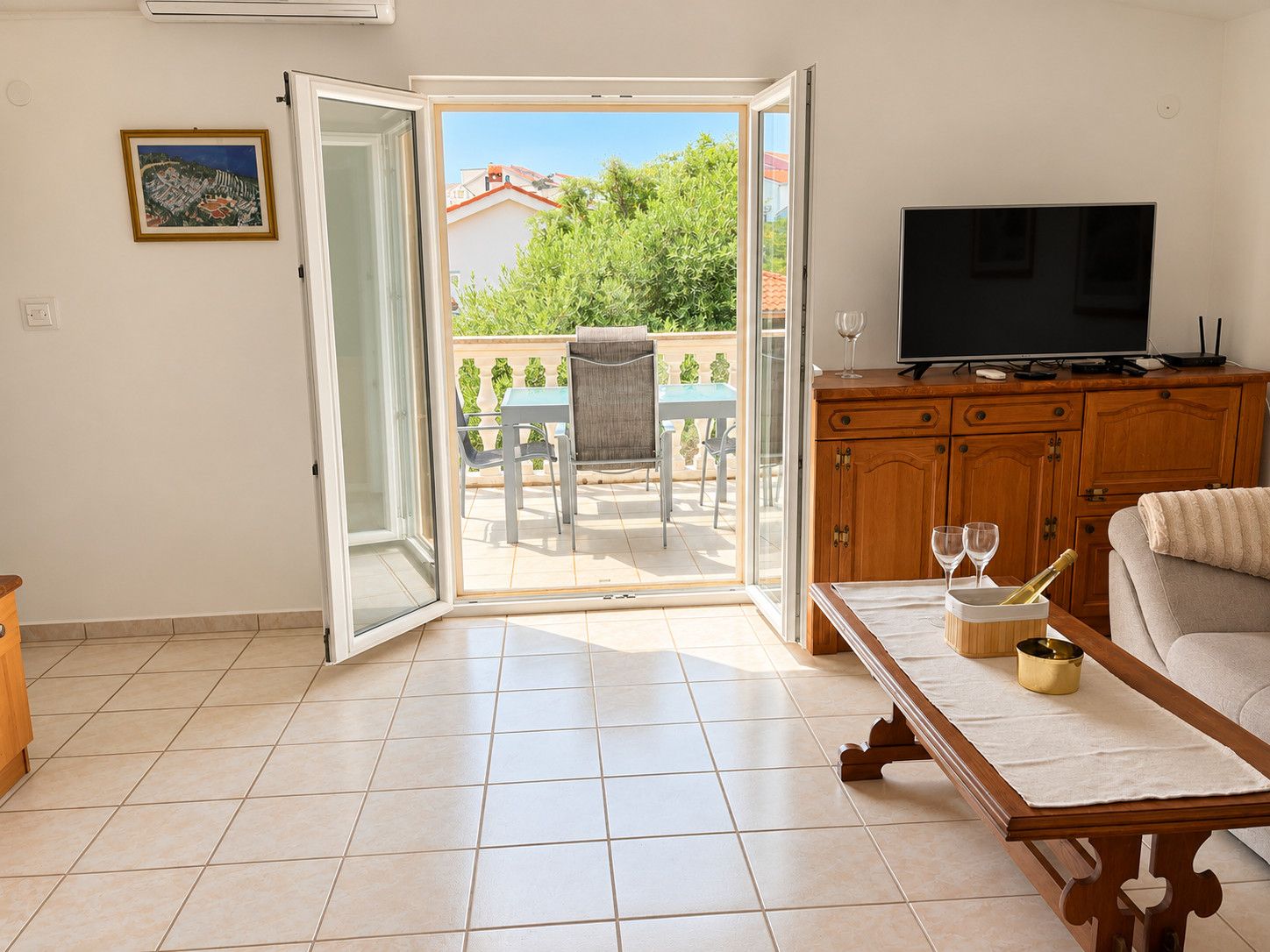 Un salon comprenant un téléviseur, un canapé, une table basse et une porte-fenêtre coulissante donnant sur une terrasse extérieure avec une table et des chaises.