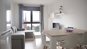 A modern living room with a sofa, a dining table with chairs, a TV, and a window with curtains.