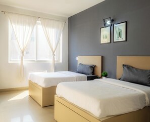 Une chambre d’hôtel avec deux lits, une fenêtre avec des rideaux, une table de chevet avec une plante et deux tableaux encadrés au mur.