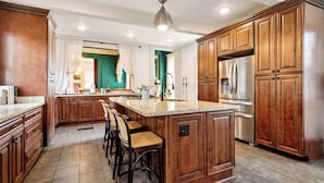 A spacious kitchen with wooden cabinets, a large island with bar stools, stainless steel appliances, and a view into the adjacent dining area.