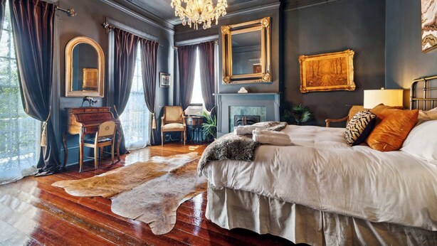 A bedroom with a large bed, a chandelier, a fireplace, and a desk with a chair.