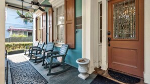 A porch with rocking chairs, a door with a decorative glass panel, and a ceiling fan.