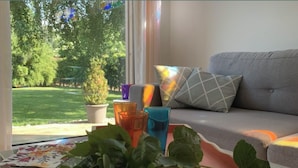 A room with a sofa, a table with colorful glasses, a potted plant, and a view of a green garden. - "Villa l'Amboise" charm and comfort**** in Baie de Somme for 10 people (PENDÉ)