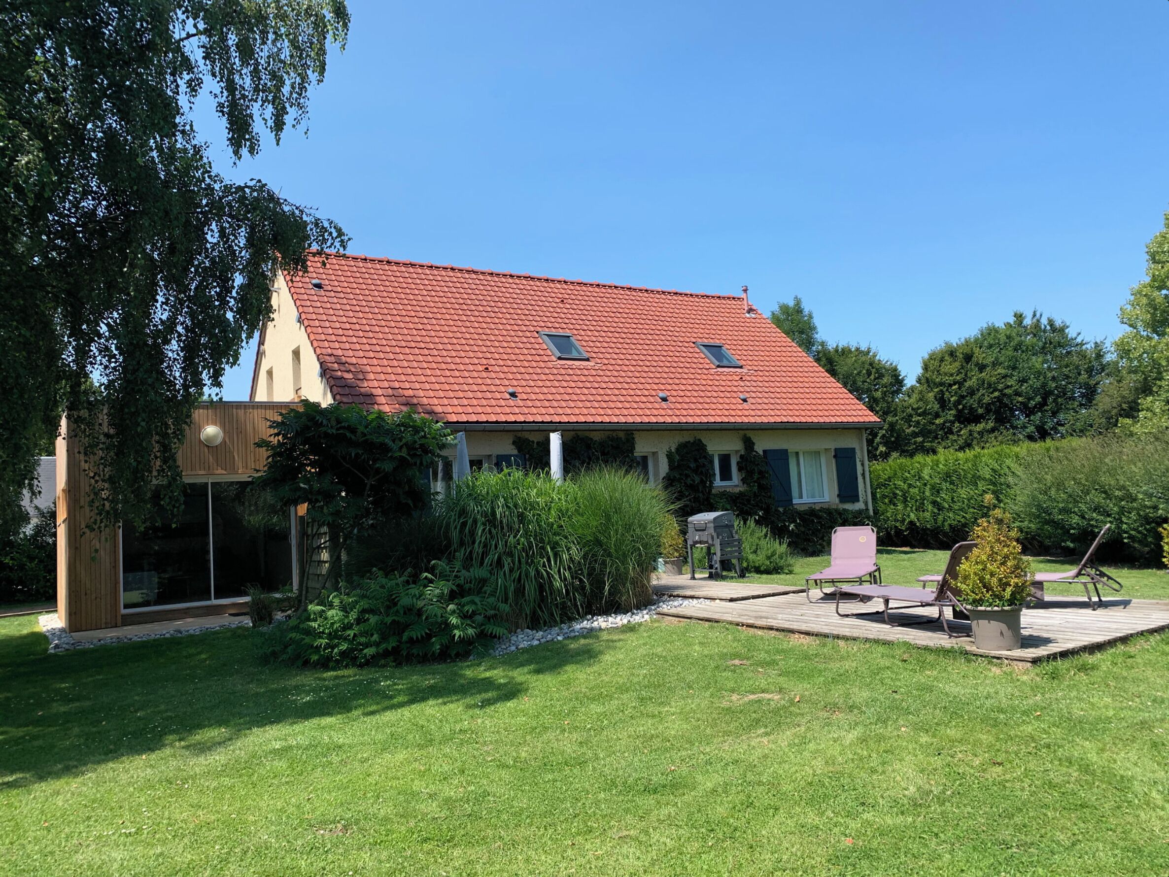 Een huis met een rode dakbedekking van pannen, een houten terras en een verzorgd gazon.