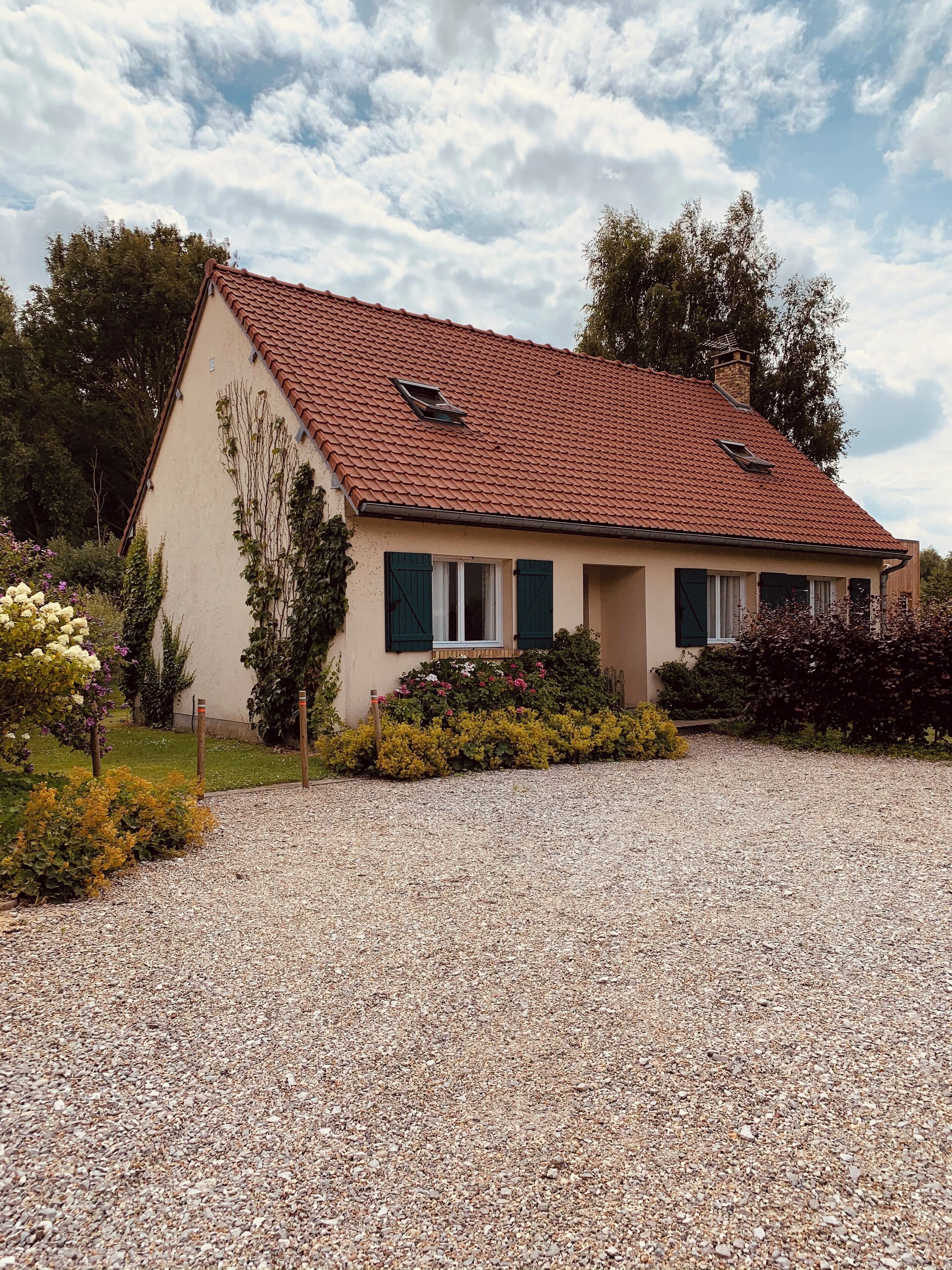 A single-story house with a red-tiled roof, a small porch, and a gravel driveway.