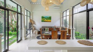 Una habitación amplia con ventanas grandes, un comedor con mesa blanca y un sofá.