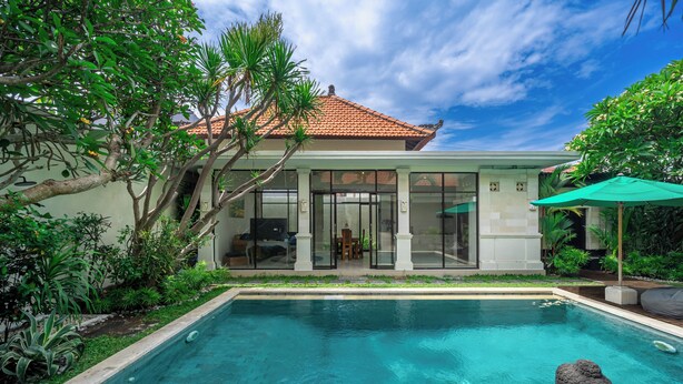 Una casa moderna con piscina, rodeada de exuberante vegetación y un cielo azul despejado.
