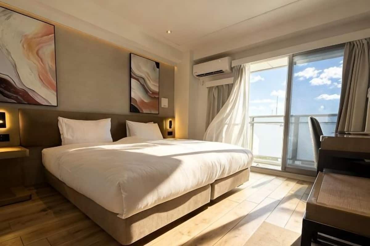 Una habitación de hotel con una cama grande, un balcón con vistas y un equipo de aire acondicionado.