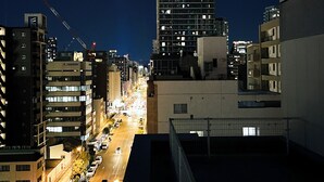 A nighttime cityscape with a prominent high-rise building, a busy street with cars, and a pedestrian crossing. - JStar Hotel Shinsaibashi (Osaka)