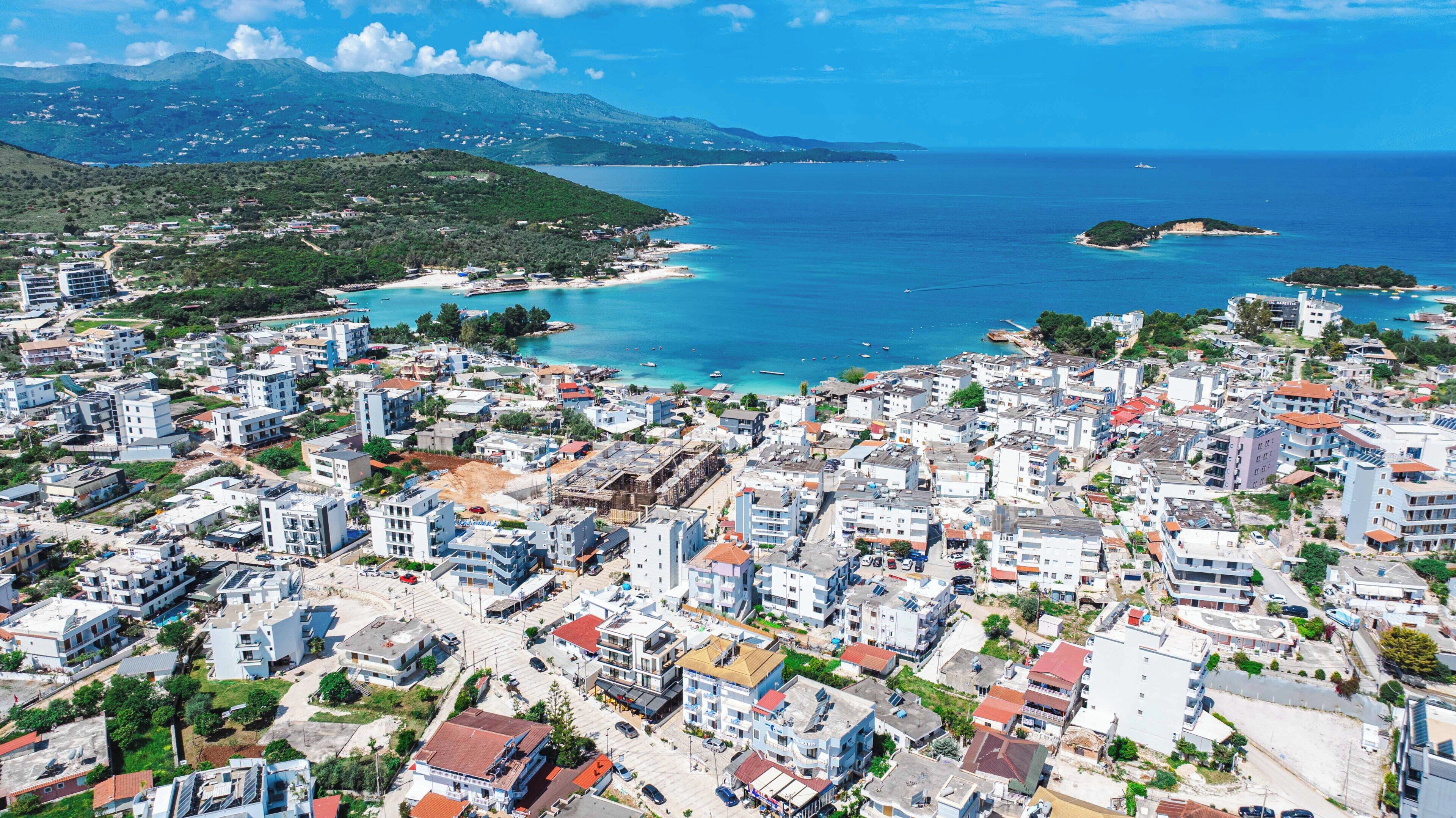 A coastal town with dense residential buildings, a marina, and a mountainous backdrop.