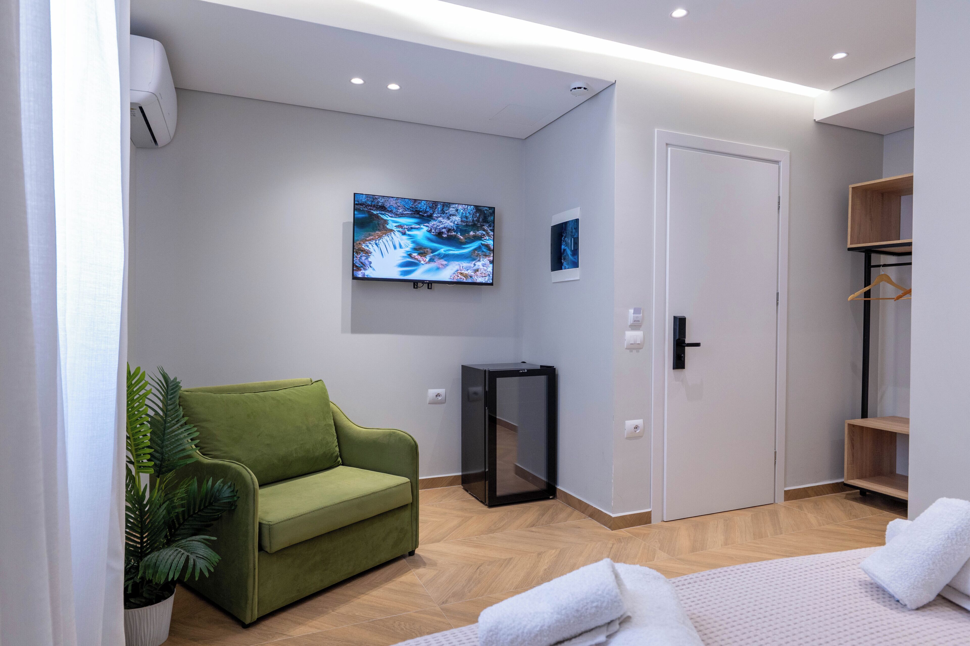 Habitación de hotel moderna con sofá verde, televisor de pantalla plana, mueble pequeño y una puerta.