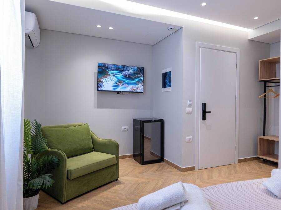 Habitación de hotel moderna con sofá verde, televisor de pantalla plana, mueble pequeño y una puerta.