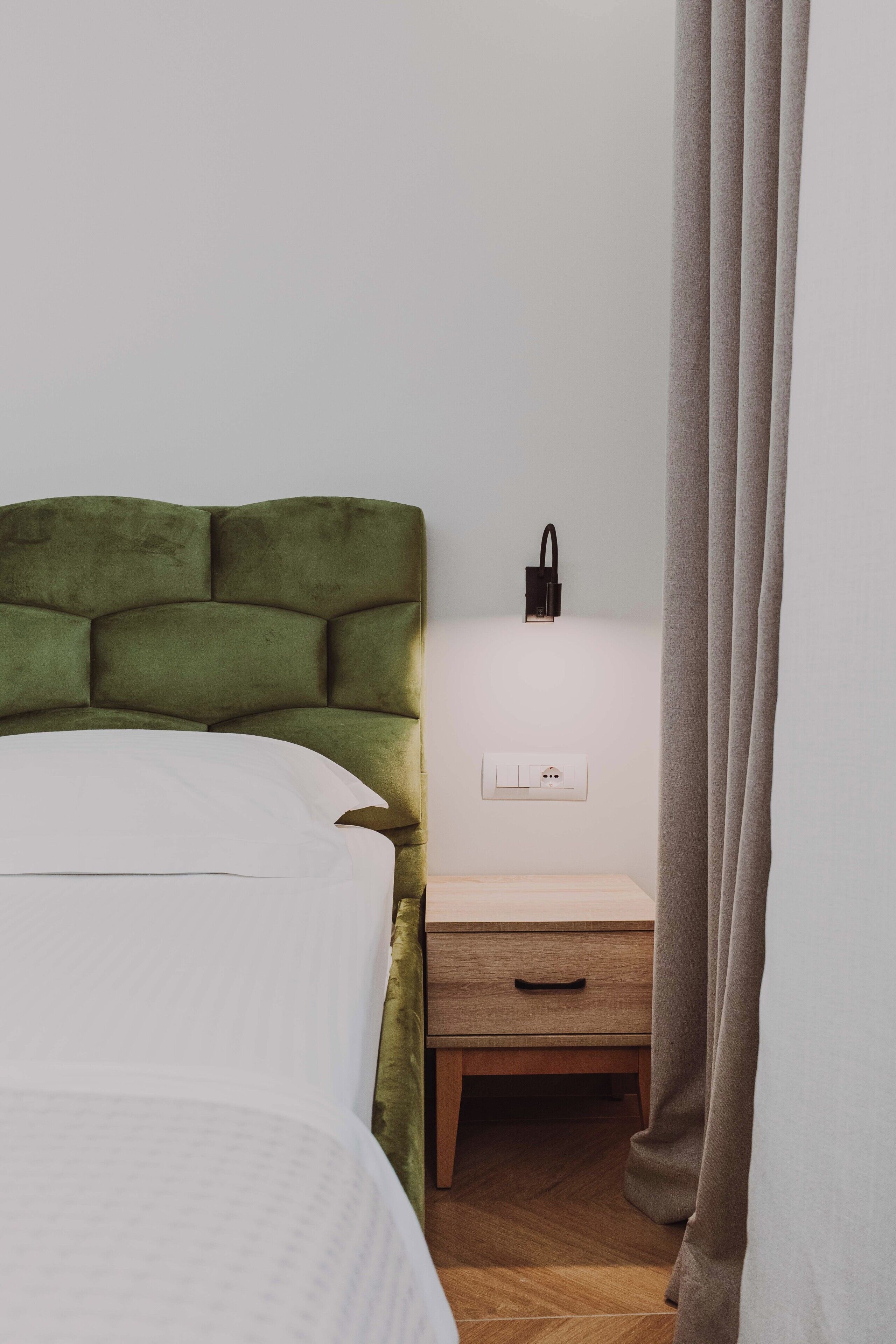 A bedroom with a green upholstered headboard, a bedside table with a lamp, and a power outlet.