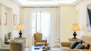 A well-lit living room with a sofa, armchairs, a coffee table, and two lamps. There is a window with curtains and a door in the background. - Boutique Abades Apartment II (Seville)
