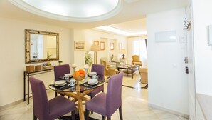 A dining area with a glass table, purple chairs, and a bowl of oranges. There is a mirror on the wall and a door to the right. - Boutique Abades Apartment II (Seville)
