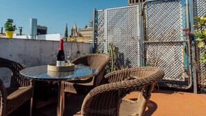 A rooftop terrace with wicker furniture, a table with a bottle and glass, and a view of a historic tower. - Boutique Abades Apartment II (Seville)
