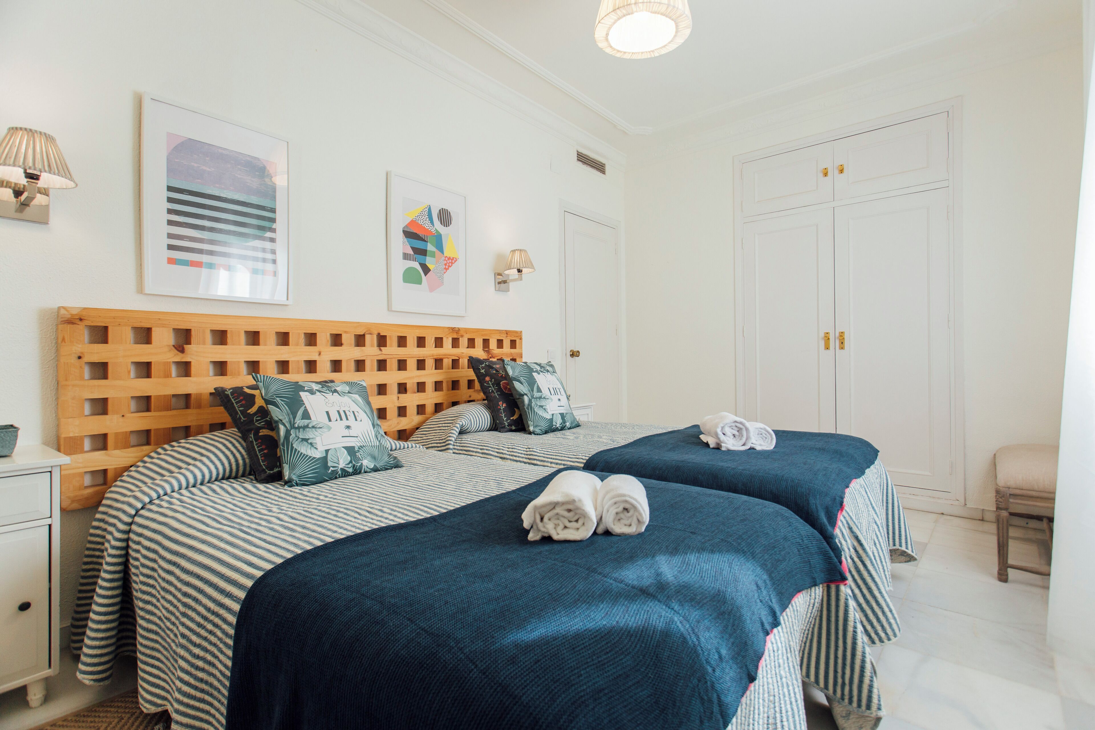A hotel room with two beds, a wooden headboard, striped bedding, and a white door.