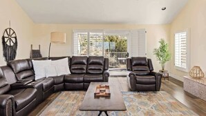 A spacious living room with a sectional sofa, a coffee table, and a view through large windows. - The Kingdom · 5000 SF Castle with Pool & Spa (Yucca Valley)