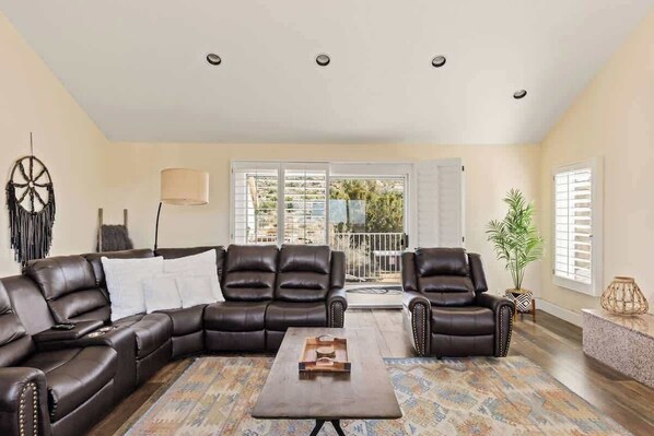 A spacious living room with a sectional sofa, a coffee table, and a view through large windows.