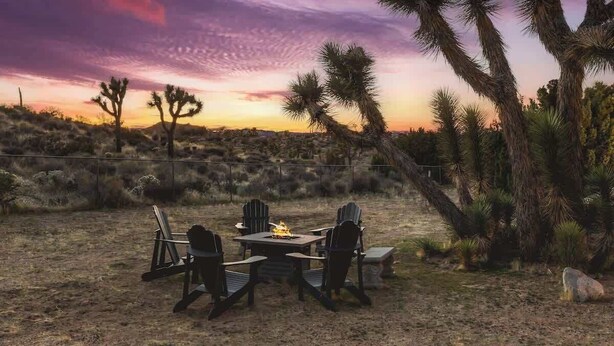 An outdoor seating area with a fire pit and chairs, surrounded by desert vegetation and a sunset sky. - The Kingdom · 5000 SF Castle with Pool & Spa (Yucca Valley)