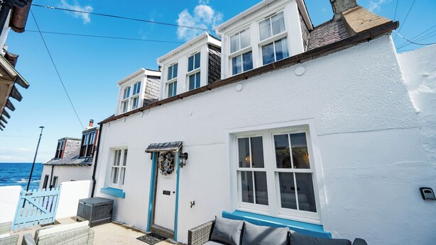 A white building with a balcony, a blue door, and a view of the sea.