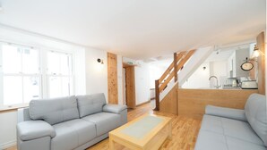 A modern living room with a grey sofa, a wooden coffee table, and a staircase leading to a kitchen area.