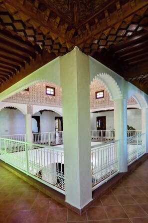An interior with ornate arches, a balcony with intricate railings, and a tiled floor.