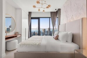 A modern bedroom with a large bed, a round mirror, a bedside table, and a view of the cityscape through large windows.